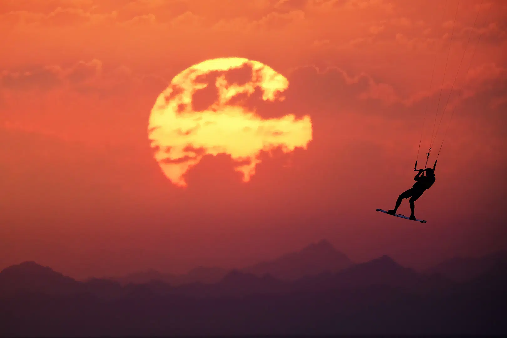 Sylwetka kitesurfera na tle pomarańczowego zachodu słońca - idealna scena na wyjazdy kitesurfingowe z KiteAway.