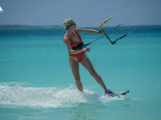 Kobieta w czerwonym stroju kitesurfinguje po turkusowej wodzie pod słońcem - radość z wyjazdu kitesurfingowego KiteAway.