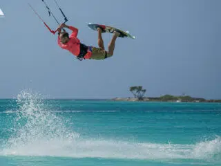 Kitesurfer w czerwonej koszulce wykonuje trick nad turkusową wodą na kite camp KiteAway - idealne wyjazdy kitesurfingowe.