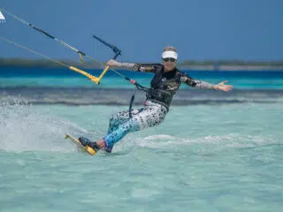 Kobieta w kolorowych legginsach kite'uje na turkusowej wodzie; idealny klimat na wyjazdy kitesurfingowe z KiteAway.