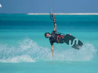Kitesurfer w kasku na turkusowej wodzie - idealna inspiracja na wyjazdy kitesurfingowe z KiteAway. Słońce i fale w tle.