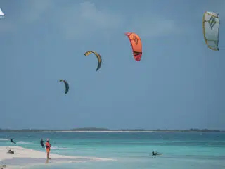 Kitesurfing na turkusowej wodzie przy piaszczystej plaży; idealny spot na wyjazdy kitesurfingowe z KiteAway.
