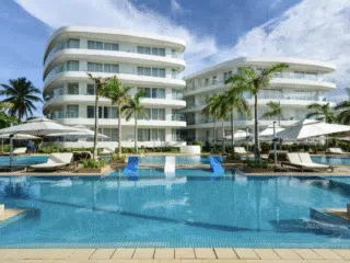 Nowoczesne białe budynki kurortu z balkonami wychodzą na błękitny basen, palmy i kitesurferów na jasnym niebie wypełnionym latawcami.