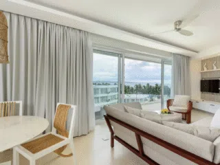 Jasny salon z widokiem na ocean, palmy i balkon - idealne miejsce na wyjazdy kitesurfingowe z KiteAway.