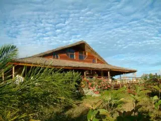 Drewniany dom z werandą i dużymi oknami wśród zieleni, idealny na kite camp z KiteAway - niezapomniane wyjazdy kitesurfingowe.