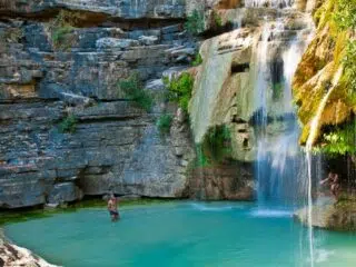 Osoba pływająca w turkusowym basenie pod wodospadem - idealny relaks po kursie kitesurfingu z KiteAway podczas wyjazdu.