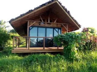 Przytulny drewniany domek przy kite spocie KiteAway otoczony zielenią, idealny na relaks po wyjazdach kitesurfingowych.