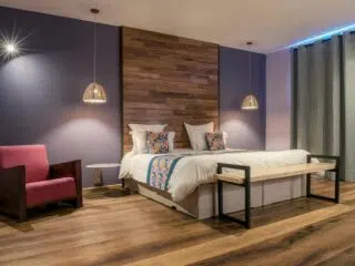 Nowoczesna sypialnia z podwójnym łóżkiem, kolorowymi poduszkami i drewnianą ścianą - idealna po wyjeździe kitesurfingowym z KiteAway.