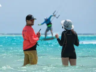 Dwie osoby stoją w płytkiej wodzie na kite camp KiteAway; w tle kurs kitesurfingu i dynamiczny kite trip na błękitnym niebie.