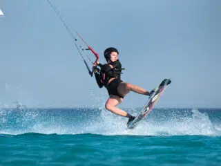 Kitesurfer unosi się nad wodą z kontrolą latawca na kempingu KiteAway - idealne wakacje z kitesurfingiem i szkoleniem latawców.