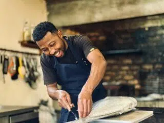 Uśmiechnięty mężczyzna w fartuchu filetującym rybę w kuchni po dniu pełnym wrażeń na kite camp z KiteAway - idealny posiłek po wyjazdach kitesurfingowych.