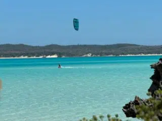 Kitesurfer na lazurowej wodzie przy piaszczystej plaży - idealne miejsce na wyjazdy kitesurfingowe z KiteAway.