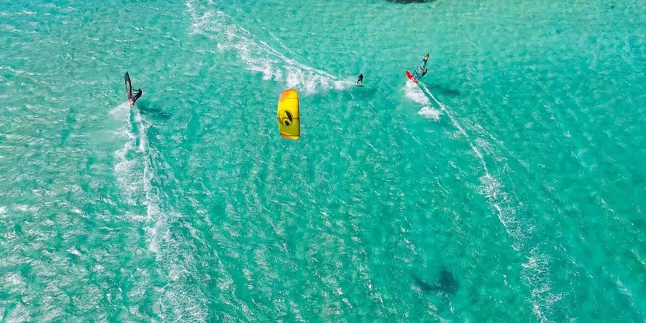 Trzech kitesurferów na turkusowej wodzie i rafach koralowych - niezapomniane wyjazdy kitesurfingowe z KiteAway.