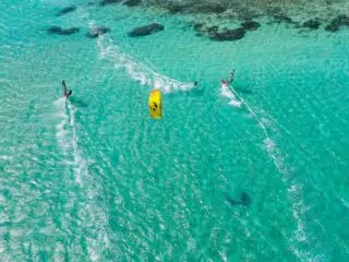 Trzech kitesurferów na turkusowej wodzie i rafach koralowych - niezapomniane wyjazdy kitesurfingowe z KiteAway.