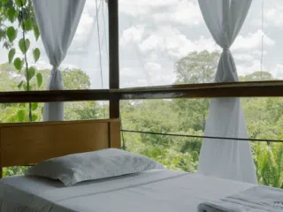 Jasne łóżko przy dużych oknach z widokiem na zieleń-idealne miejsce na regenerację podczas wyjazdu kitesurfingowego z KiteAway.