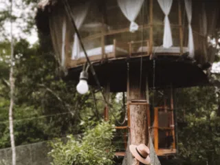 Osoba w kapeluszu idzie po wiszącym moście do domku na drzewie-idealne miejsce na relaks po kursie kitesurfingu z KiteAway.