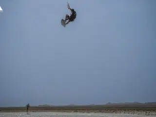 Kitesurfer unosi się nad plażą na wakacjach z kitesurfingiem z KiteAway, idealnym spotem z pięknym niebem i szkoleniem latawców.