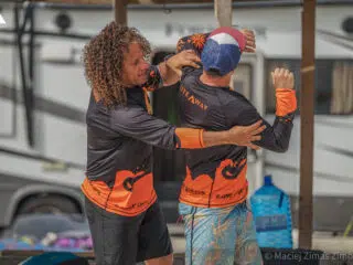 Dwóch mężczyzn w koszulkach KiteAway rozmawia przy kamperze podczas kite tripu. Wyjazdy kitesurfingowe z KiteAway.