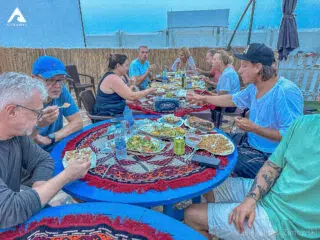 Uczestnicy wyjazdu KiteAway jedzą razem posiłek przy niebieskim stole po dniu pełnym wrażeń na kursie kitesurfingu.