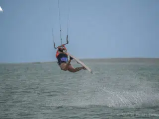 Kitesurfer w powietrzu nad spokojnym morzem, idealne wakacje z kitesurfingiem i kite camp z KiteAway pod pochmurnym niebem.