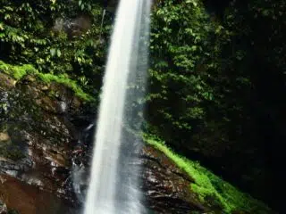 Wysoki wodospad spływa po zielonych skałach; uczestnik KiteAway odpoczywa, planując wyjazdy kitesurfingowe i kite camp.