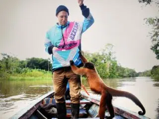 Osoba na łódce w kolorowej kurtce, małpka zagląda do kieszeni; tropikalna sceneria idealna na wyjazdy kitesurfingowe z KiteAway.