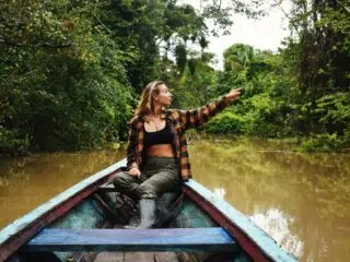 Kobieta na łódce na rzece w dżungli podczas wyjazdu kitesurfingowego z KiteAway, wskazuje na drzewa; przygoda kite trip.