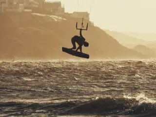 Kitesurfer wykonuje trik nad falami o zachodzie słońca - idealne wakacje z kitesurfingiem KiteAway, najlepsze wyjazdy kitesurfingowe.