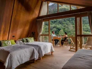 Przytulny pokój w drewnianym domku z widokiem na las; para odpoczywa po dniu pełnym emocji na kite camp z KiteAway.