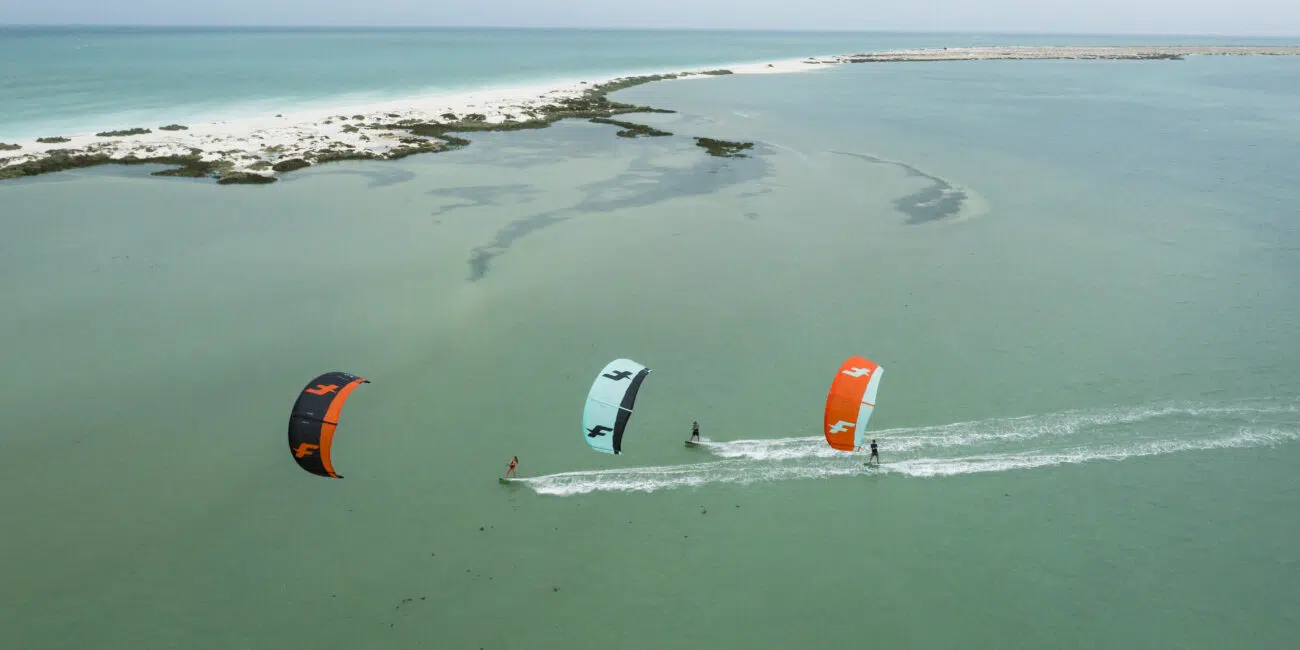 Trzech kitesurferów na turkusowej wodzie obok piaszczystej wyspy-idealne miejsce na wyjazdy kitesurfingowe z KiteAway.