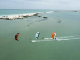 Trzech kitesurferów na turkusowej wodzie obok piaszczystej wyspy-idealne miejsce na wyjazdy kitesurfingowe z KiteAway.