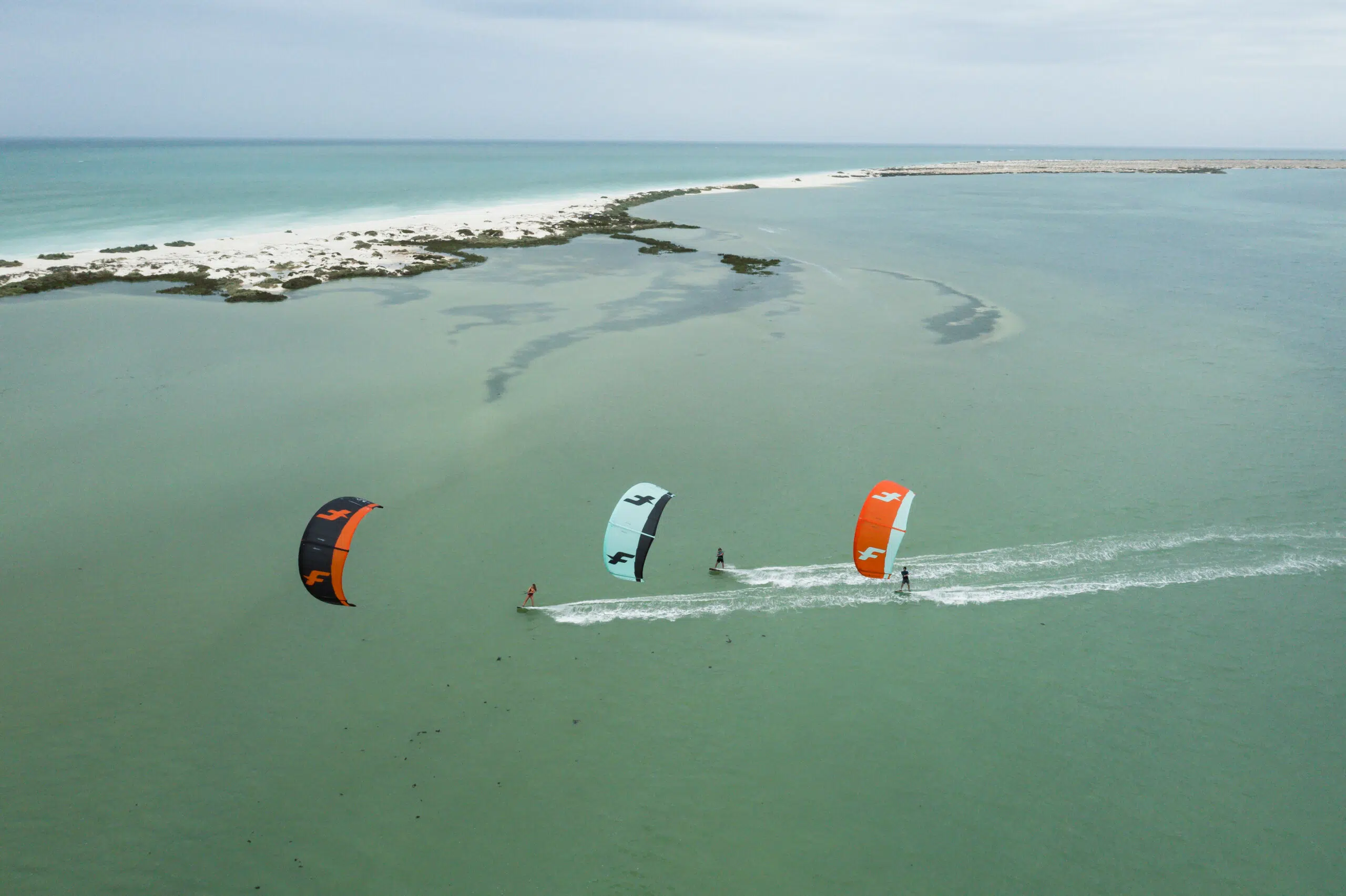 Trzech kitesurferów na turkusowej wodzie obok piaszczystej wyspy-idealne miejsce na wyjazdy kitesurfingowe z KiteAway.