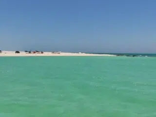 Turkusowa woda i piaszczysta plaża z łódkami-idealny spot kite na wyjazdy kitesurfingowe lub kurs kitesurfingu z KiteAway.