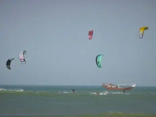Pięciu kitesurferów pływa przy drewnianej łodzi na niebieskim oceanie-idealny kite spot na wyjazdy kitesurfingowe z KiteAway.