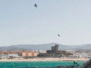 Kitesurfer leci nad turkusową wodą przy piaszczystej plaży, idealne miejsce na wyjazdy kitesurfingowe z KiteAway.