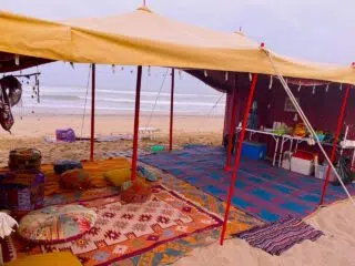 Żółty namiot na plaży z kolorowymi dywanami, poduchami i przekąskami - idealny kite camp z KiteAway, wakacje z kitesurfingiem.