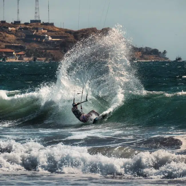 Kitesurfer na fali tworzy dużą bryzę w słoneczny dzień - idealne miejsce na wyjazdy kitesurfingowe z KiteAway.pl.