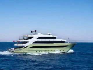 Przestronny biało-jasnozielony jacht pływa po głębokiej, błękitnej wodzie, idealnej na wyprawę kitesurfingową, z górami na horyzoncie.