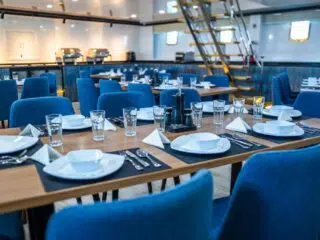 Nowoczesna jadalnia z drewnianymi stołami, niebieskimi krzesłami-miejsce spotkań po kite campie z KiteAway. Idealne na wyjazdy kitesurfingowe.